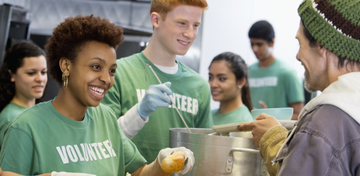 People wearing green shirts that say "Volunteer" and are handing out food to other people