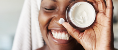 img title A woman hold up a small jar of moisturizer to her left eye while smiling
